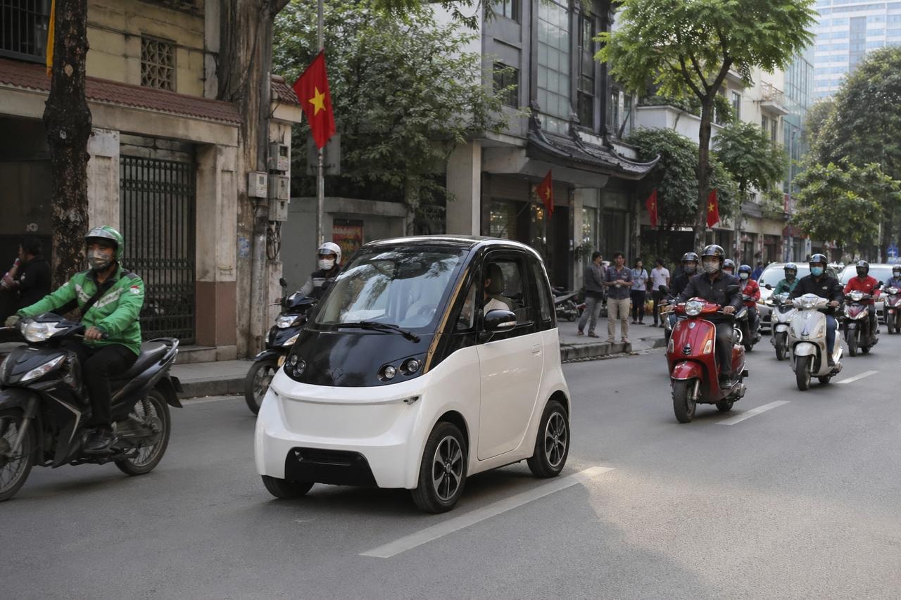 سيارة كهربائية صغيرة تسير في شارع مزدحم بالدراجات النارية في مدينة آسيوية