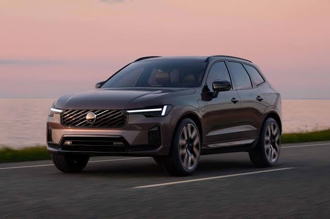 A modern Volvo plug-in hybrid SUV driving smoothly on a scenic coastal road at sunset, highlighting its advanced design and electric capabilities